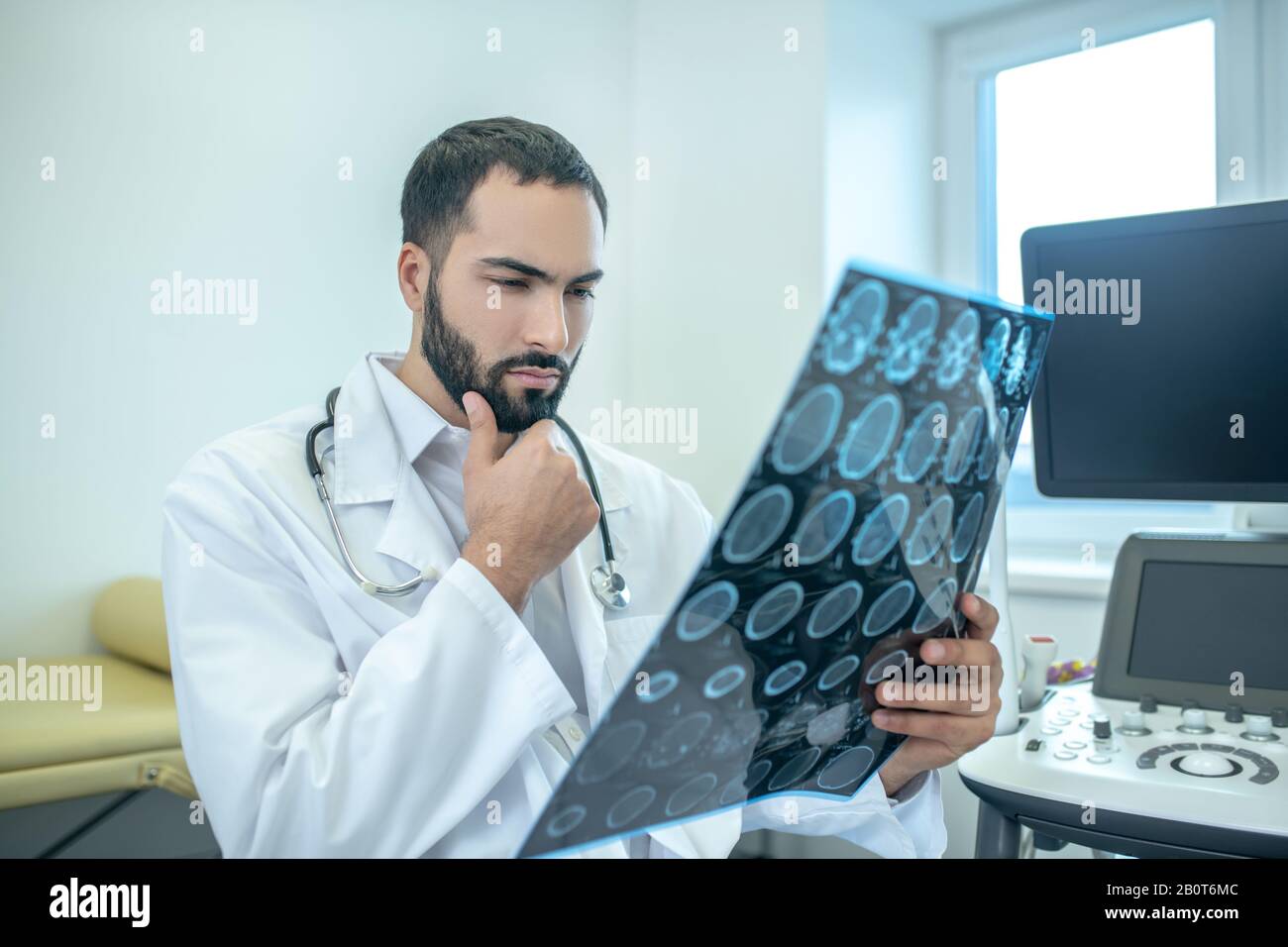 Male bearded doctor in a white robe analyzing MRI results looking serious Stock Photo