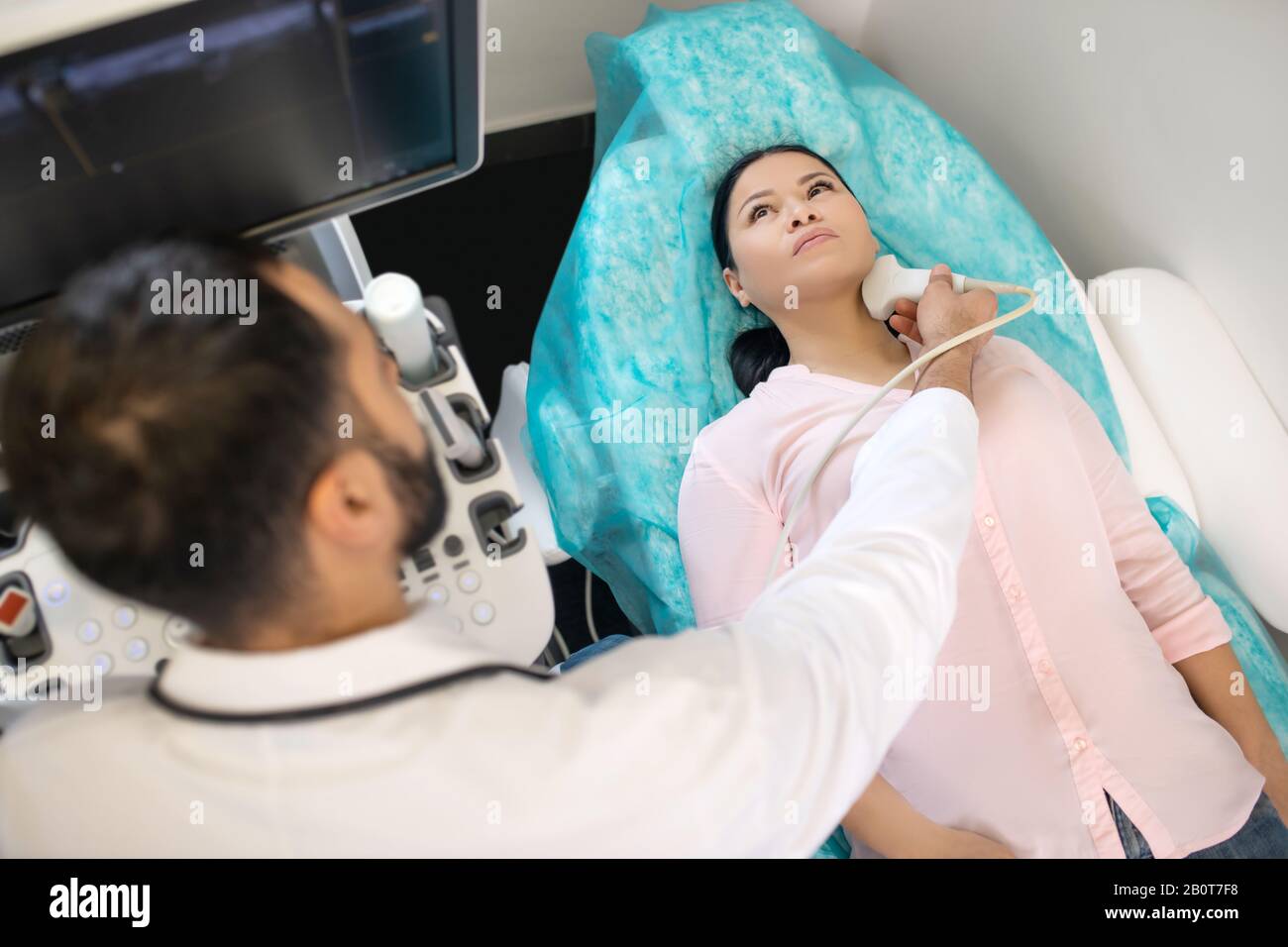 Asian woman laying on the couch having ultrasonic investigation of neck lymph nodes Stock Photo