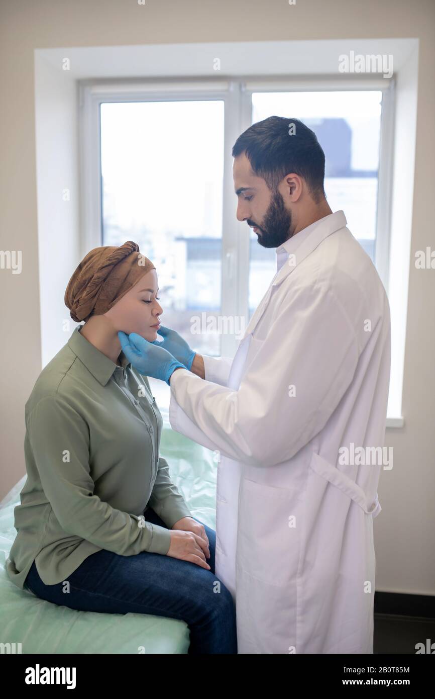 Tall doctor in blue gloves palping lymph nodes of female patient Stock Photo