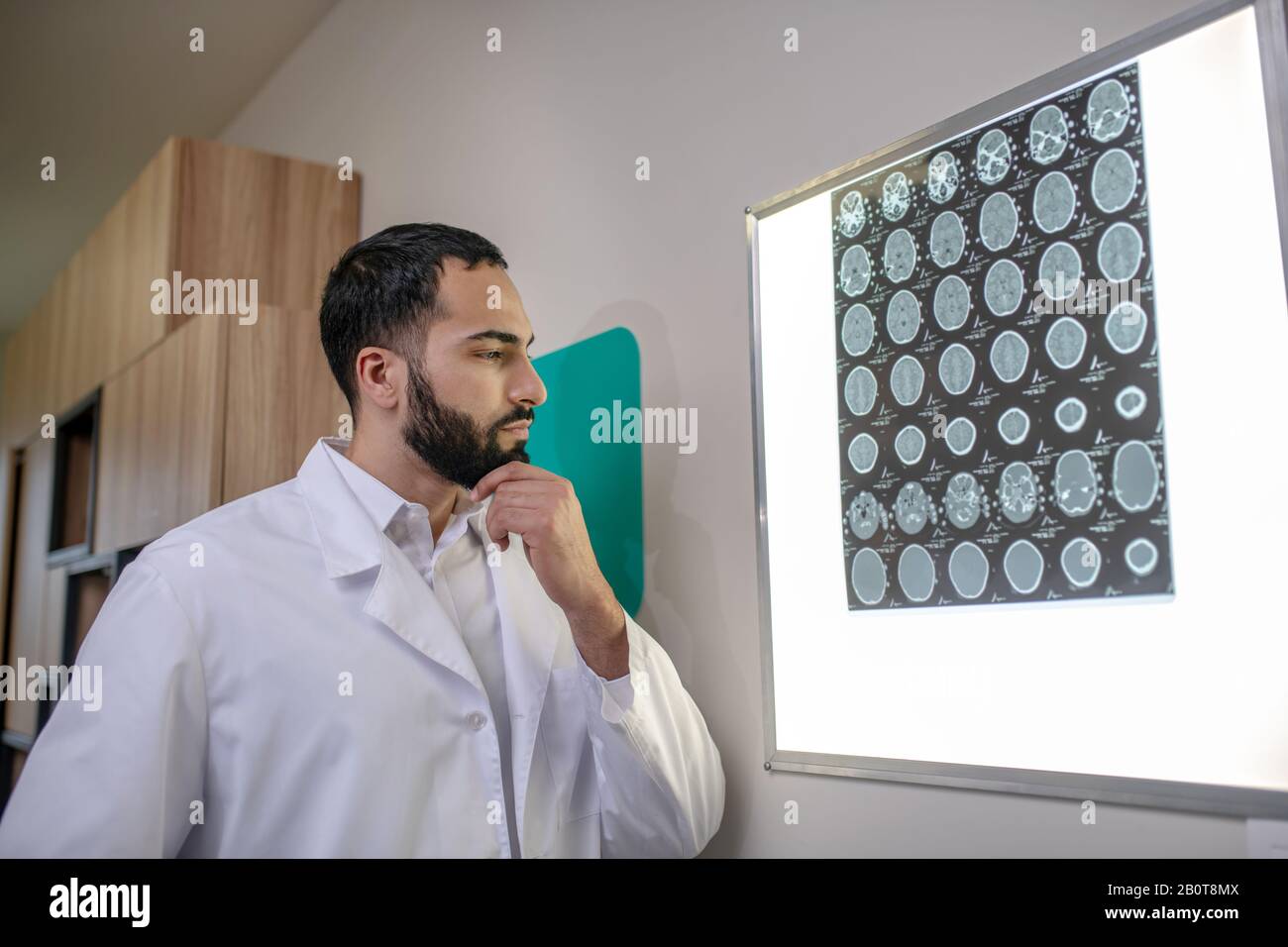 Bearded young doctor looking thoughtful while analyzing MRI results Stock Photo