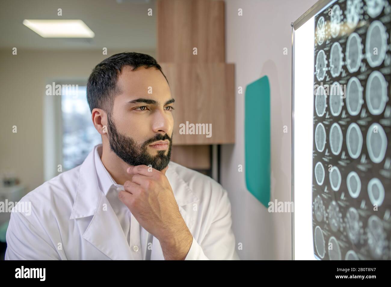 Bearded young doctor in a white robe analyzing MRI results Stock Photo