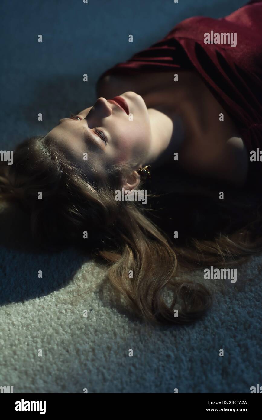 Dead woman with blonde hair in red dress on white carpet Stock Photo