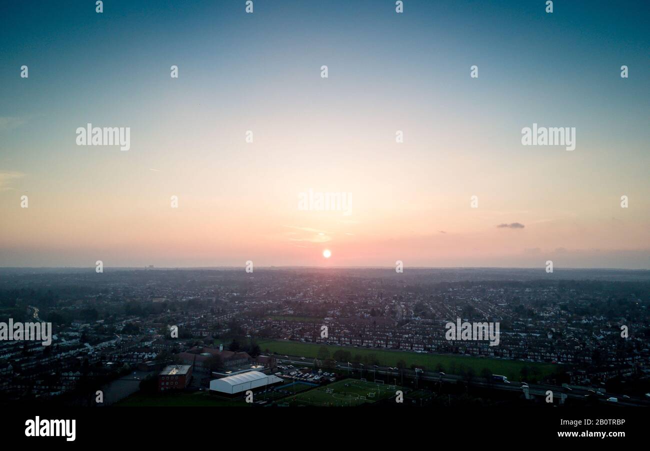 Suburban London sunset. A low setting sun resting over the horizon of a clear sky with rows of houses in the North London haze. Stock Photo