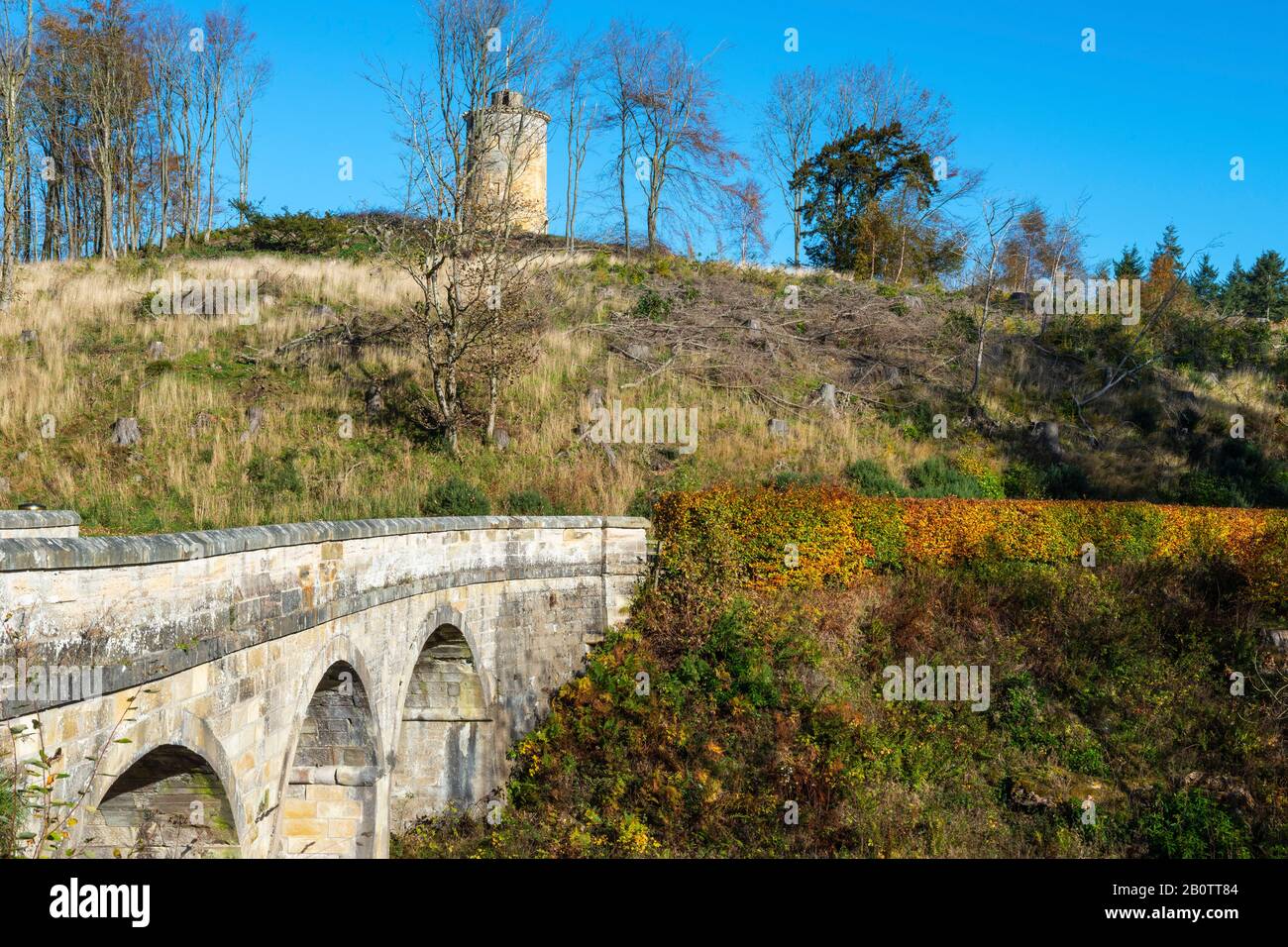 Stone arch bridge on main entrance driveway with Knight’s Law Tower in background, Penicuik Estate, Midlothian, Scotland, United Kingdom Stock Photo