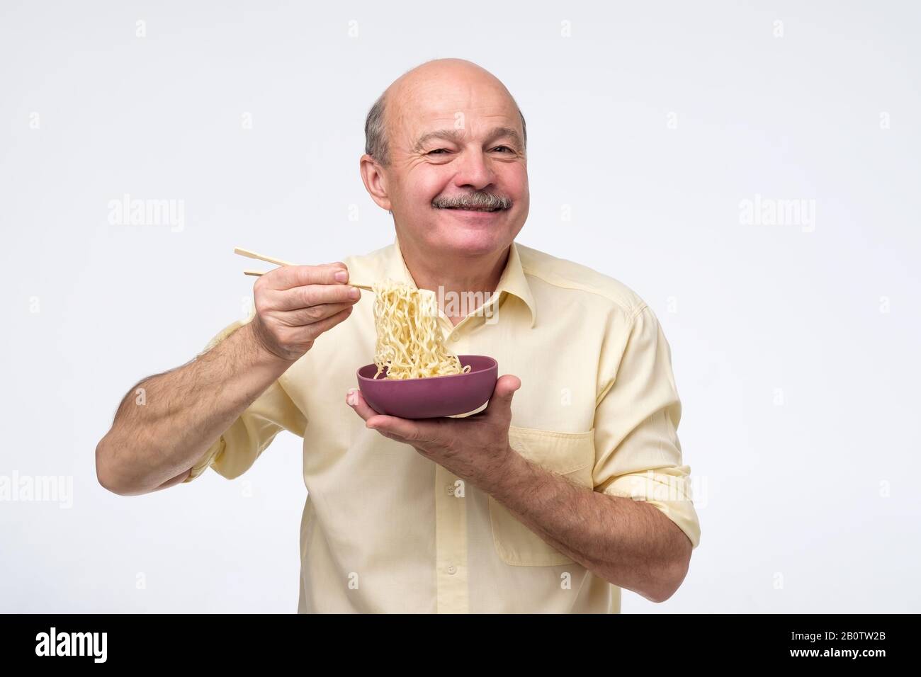 Senior bald asian man eating noodles, traditional chinese food. Quick dinner concept. Stock Photo