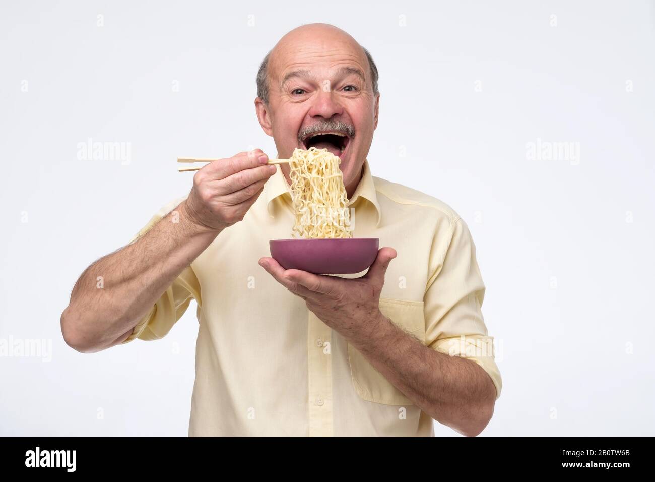 Senior bald asian man eating noodles, traditional chinese food. Quick dinner concept. Stock Photo