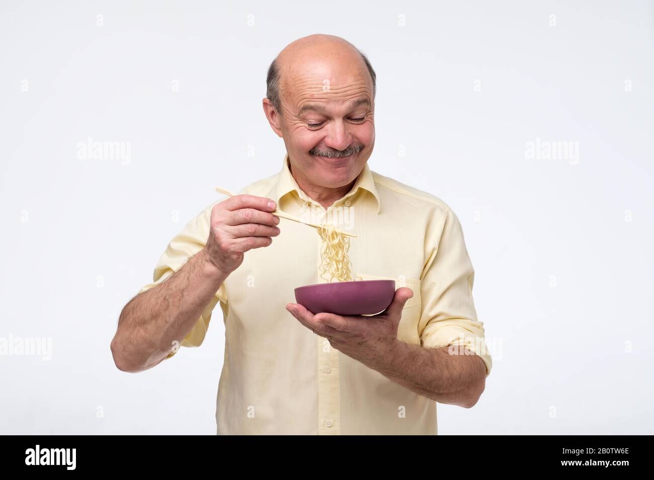 Senior bald asian man eating noodles, traditional chinese food. Quick dinner concept. Stock Photo