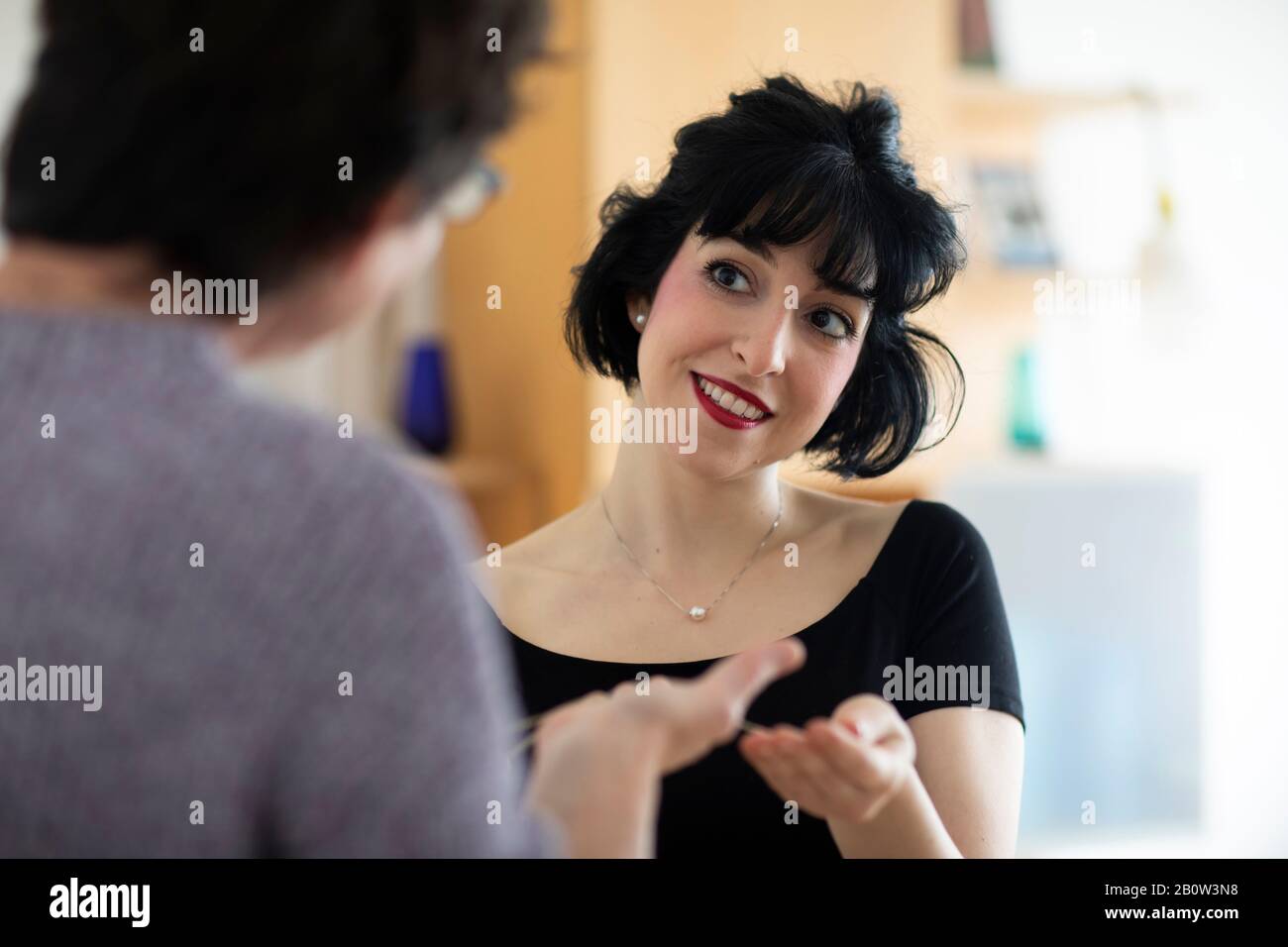 Smiling woman with black hair sitting at table, talking to a friend. Stock Photo