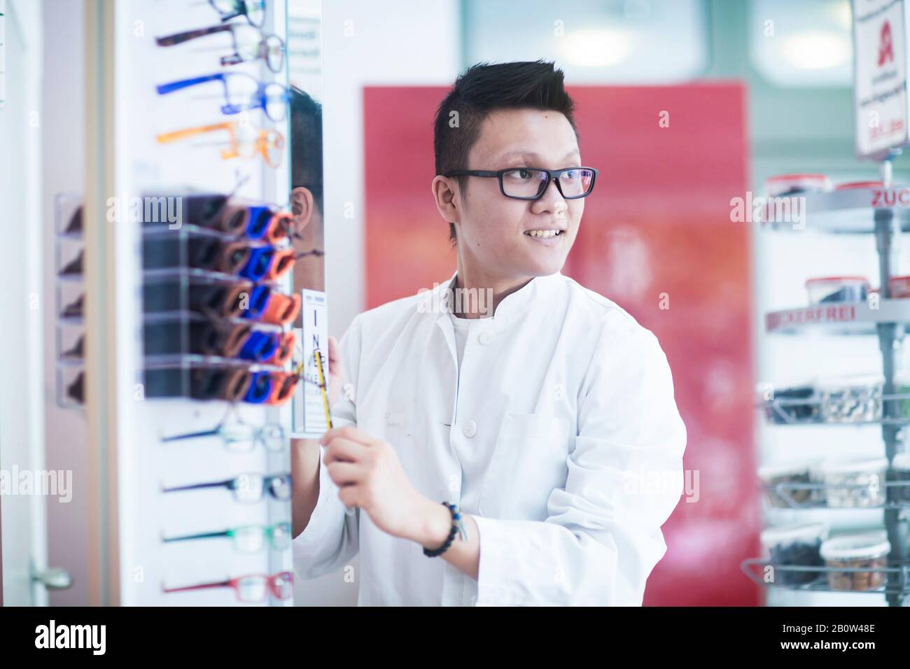 Male Asian pharmacist wearing glasses standing next to a display of