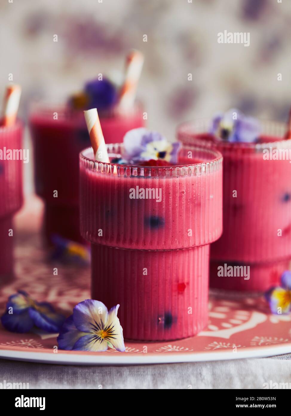 Close up of three glasses of pink smoothie decorated with pansy petals. Stock Photo
