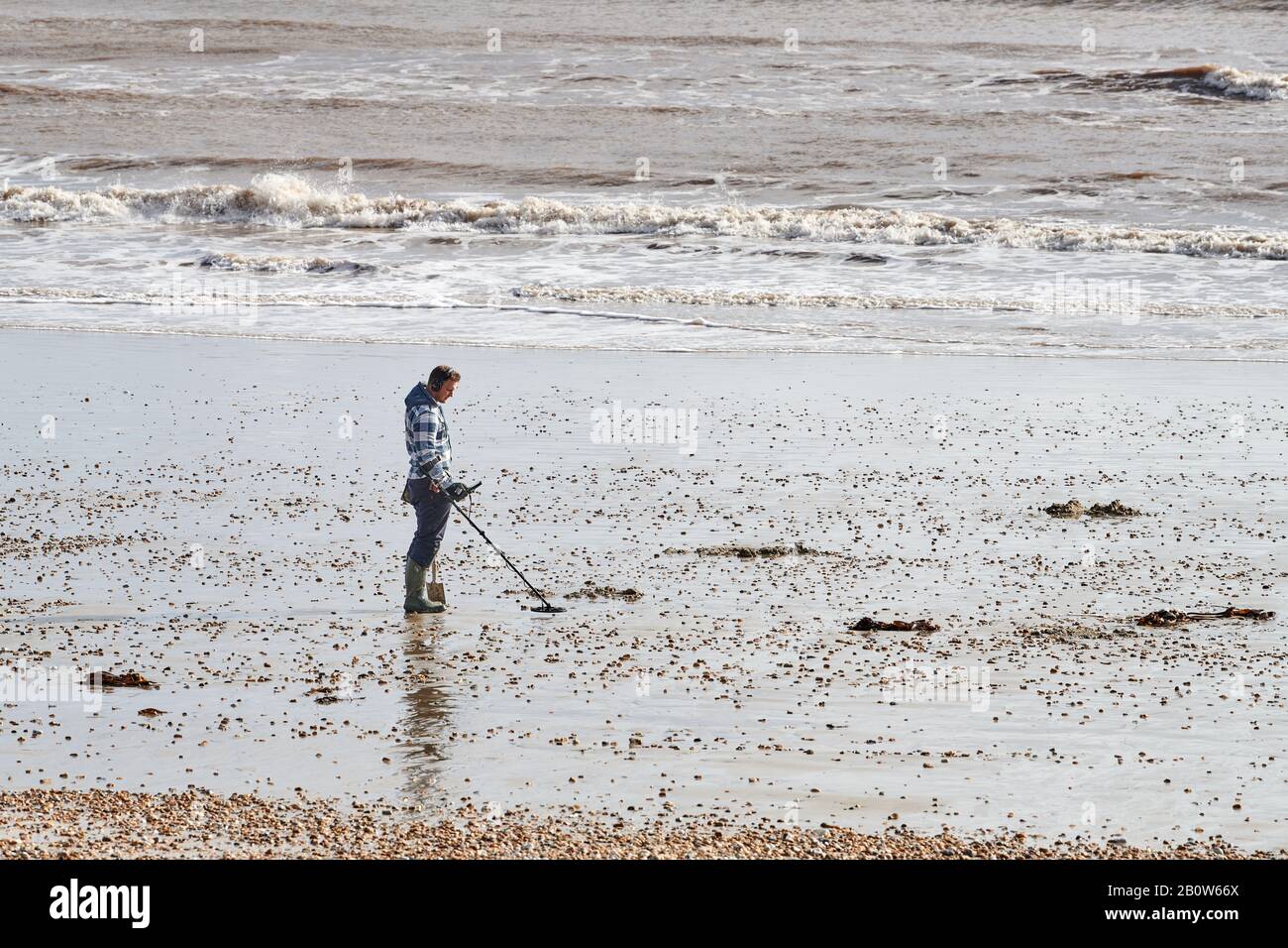 Beachcomber with metal detector on the shingle beach of Lyme Bay, Lyme Regis, Dorset, England, on a winter day. Stock Photo