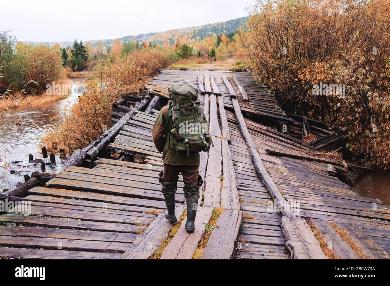 Angler crossing collapsed wooden bridge, Ural, Russia Stock Photo