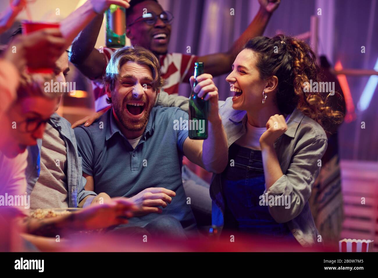 Happy young friends drinking beer and happy for their football team during watching a match on TV Stock Photo