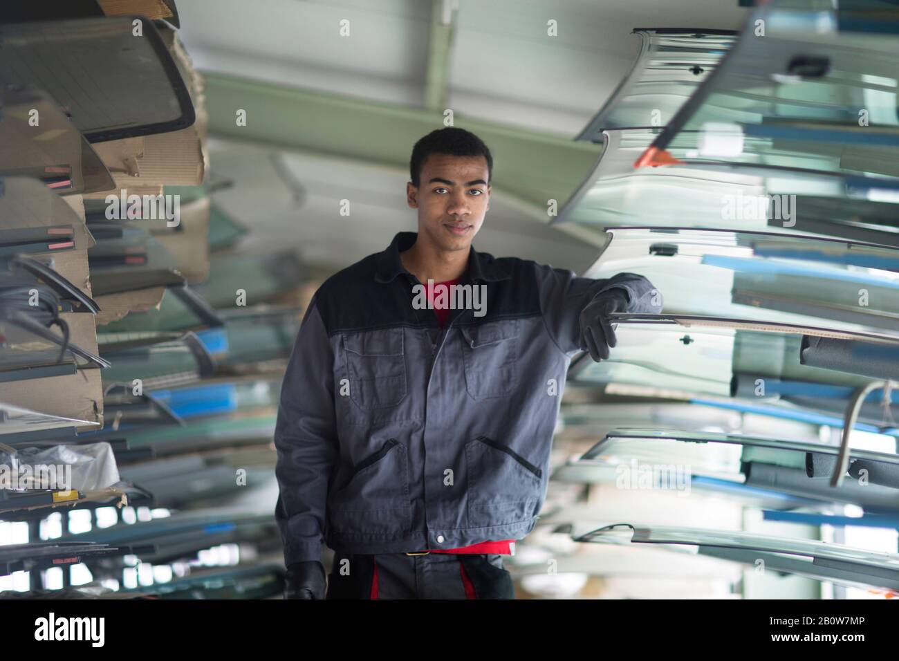 Workman leaning against stack of car windshield in workshop Stock Photo