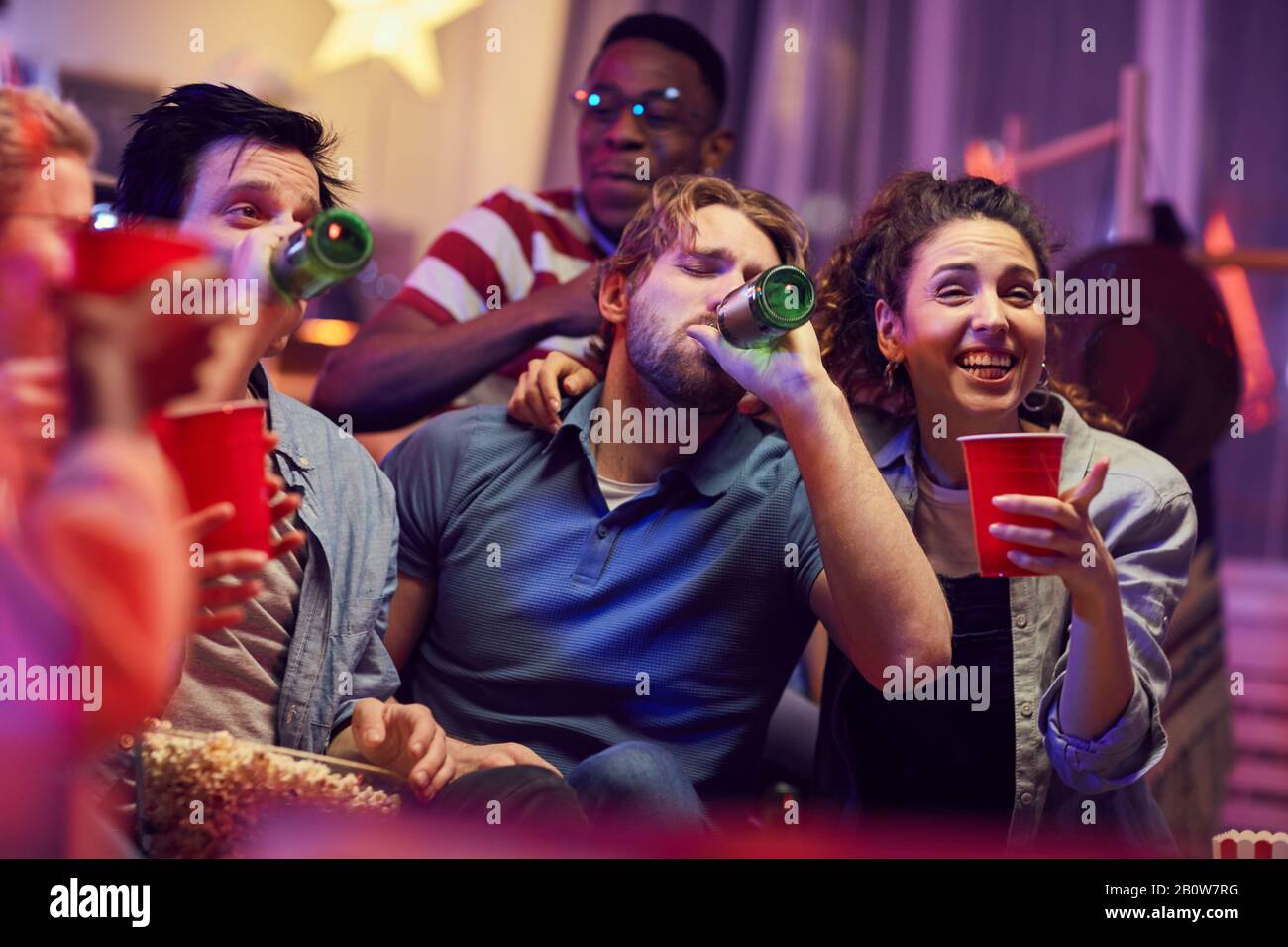 Young men drinking beer from bottles while sitting on sofa together ...