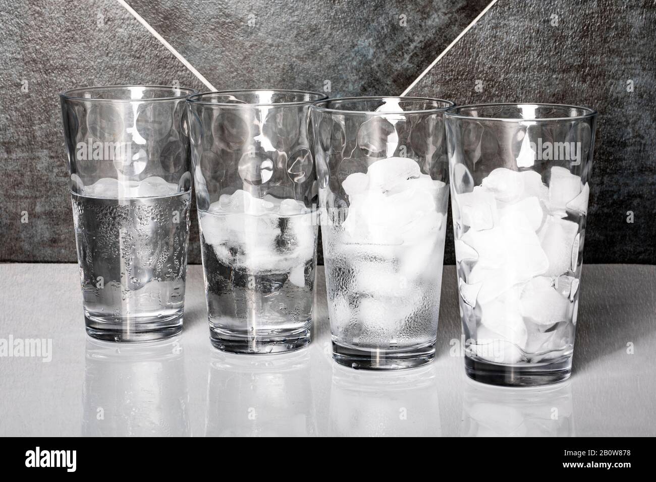 View of four glasses of ice on a table top, each at a different stage of melting. Stock Photo