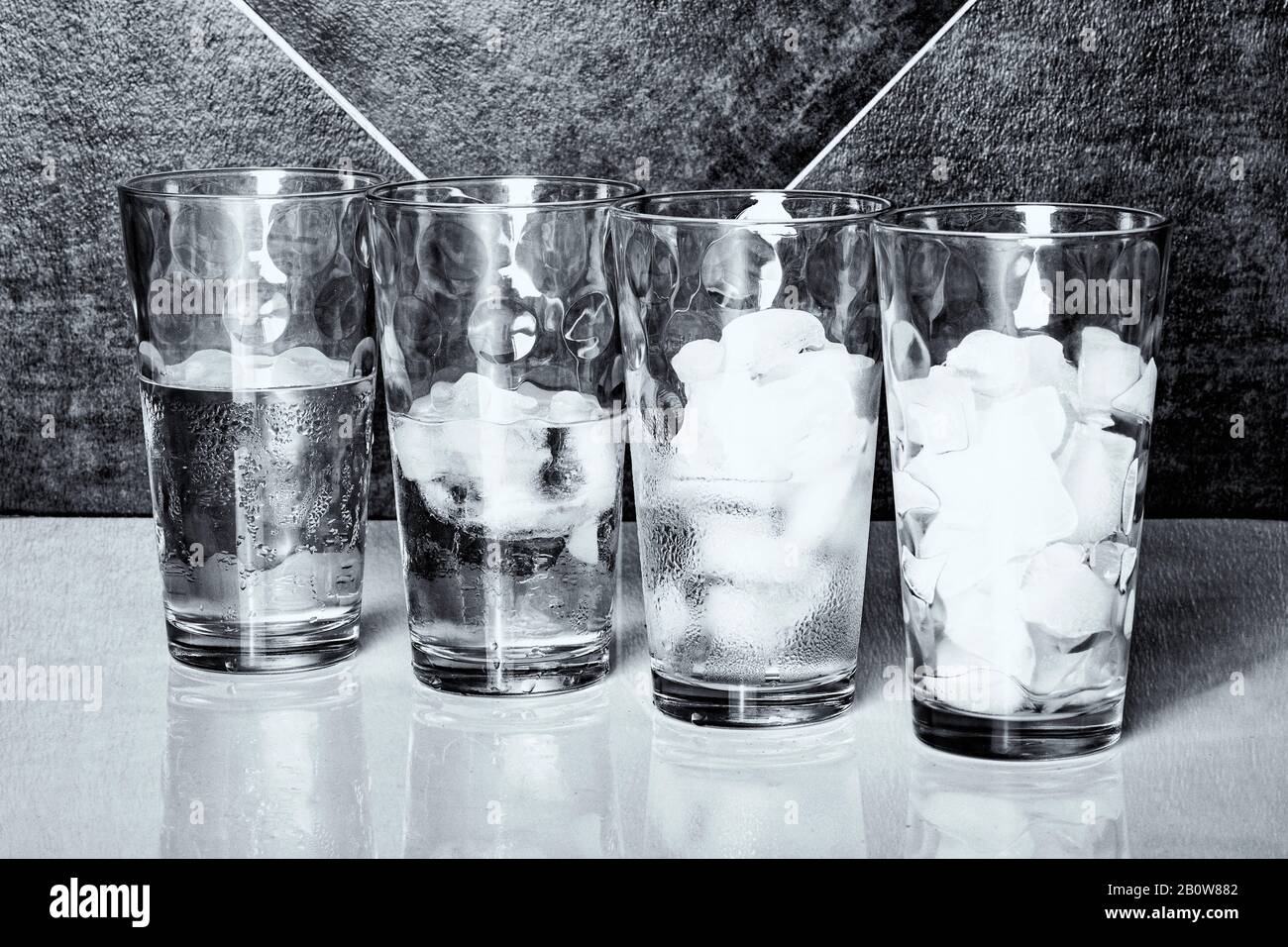 Monochrome view of four glasses of ice on a table top, each at a different stage of melting. Stock Photo