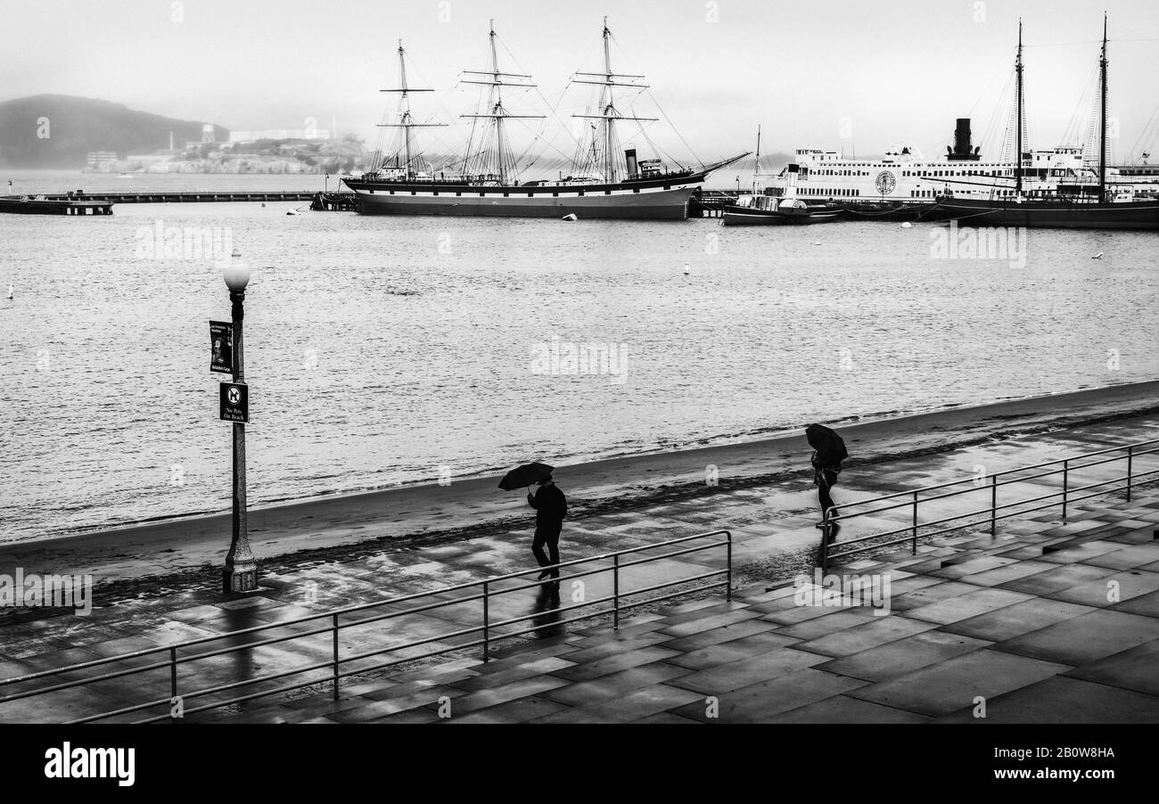 A view glancing over the tops of two umbrellas on a rainy day towards the old boats of the maritime national historic park and Alcatraz to the left. Stock Photo