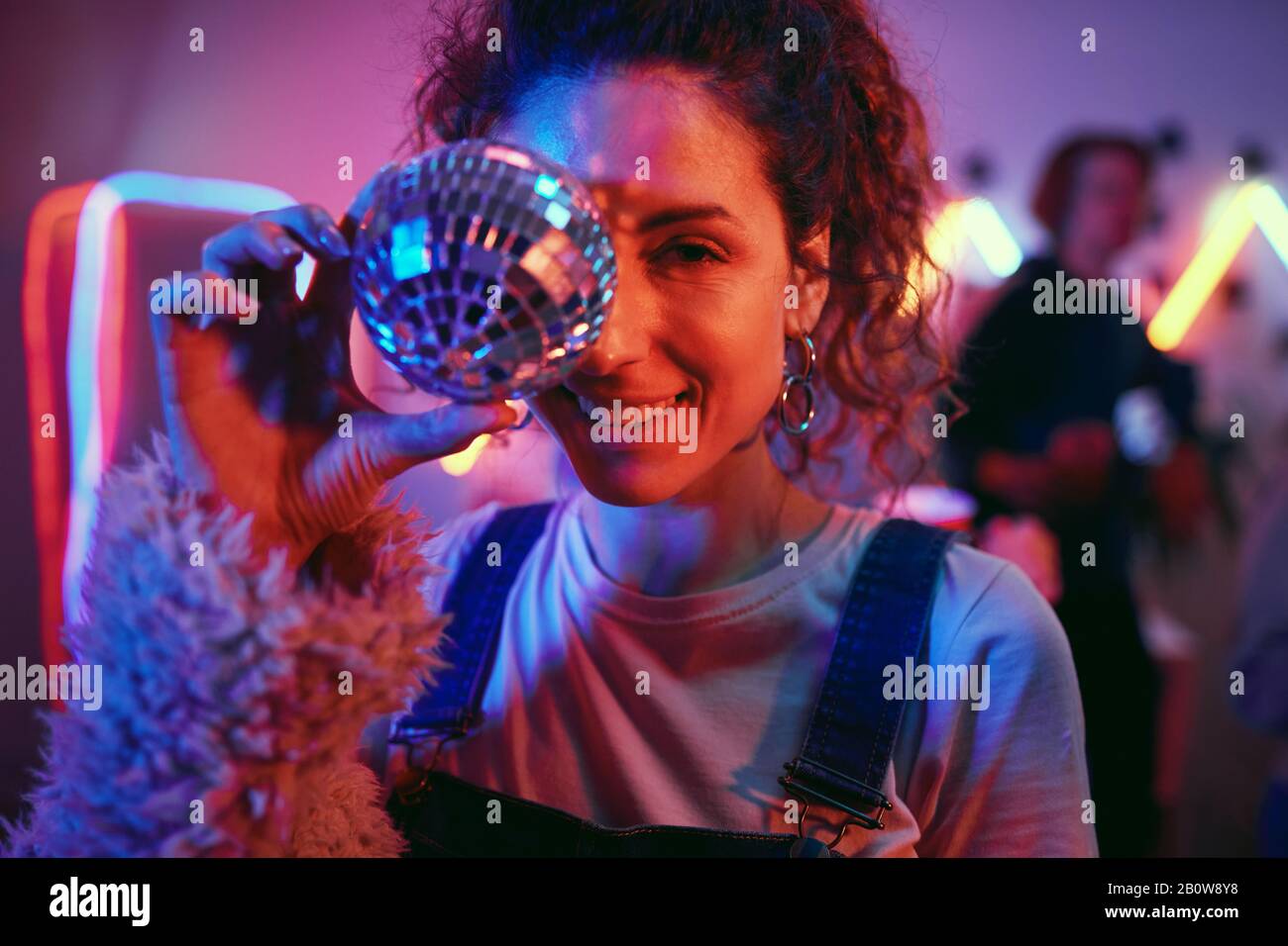 Portrait of beautiful smiling woman posing at camera with disco ball during disco party Stock Photo