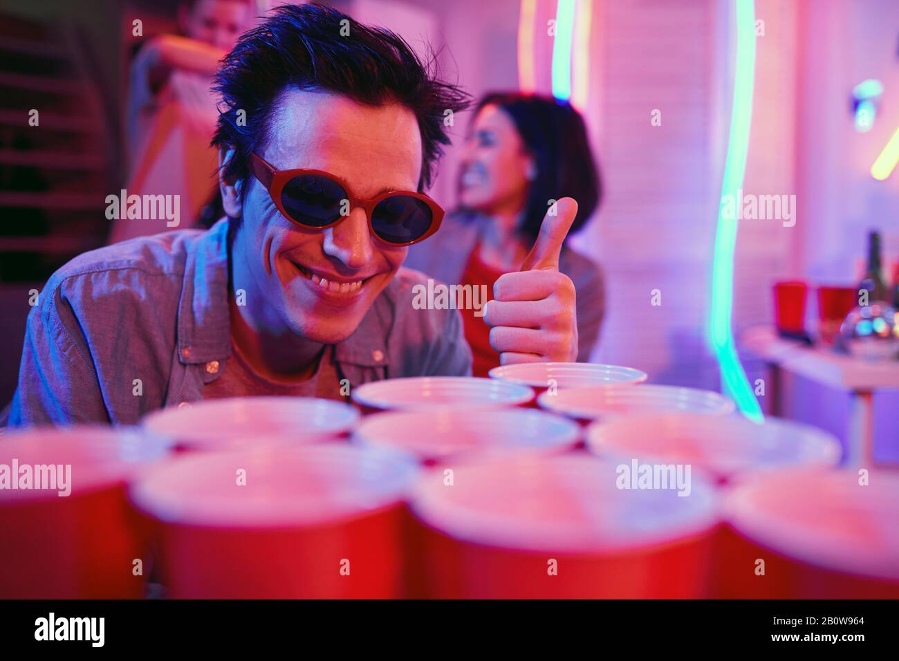 Young happy boy in sunglasses showing thumb up and smiling at camera while standing near the drinks at party Stock Photo