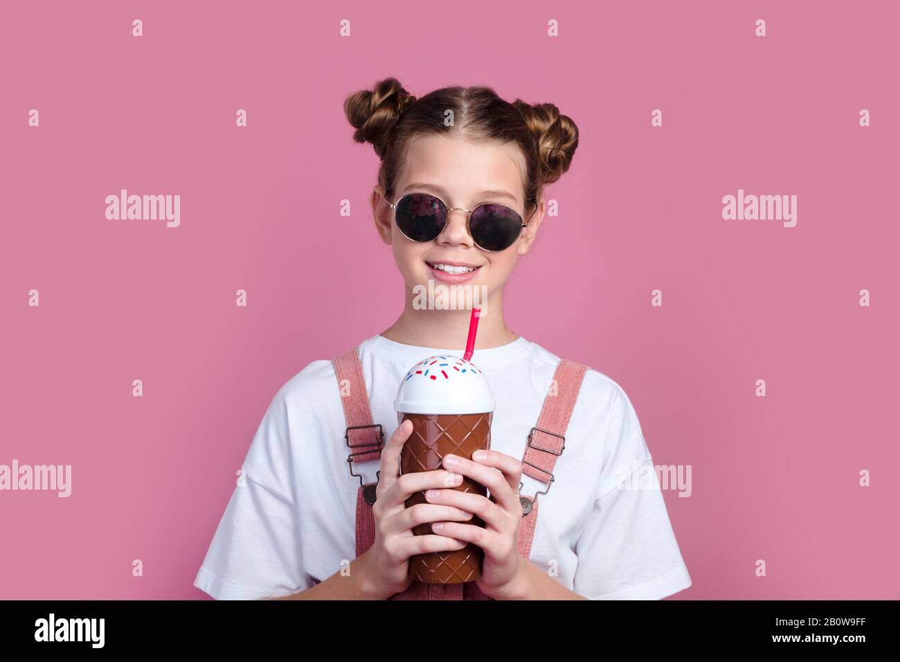 Pretty little girl in casual clothes and sunglasses on pink with cocktail chilling. Stock Photo