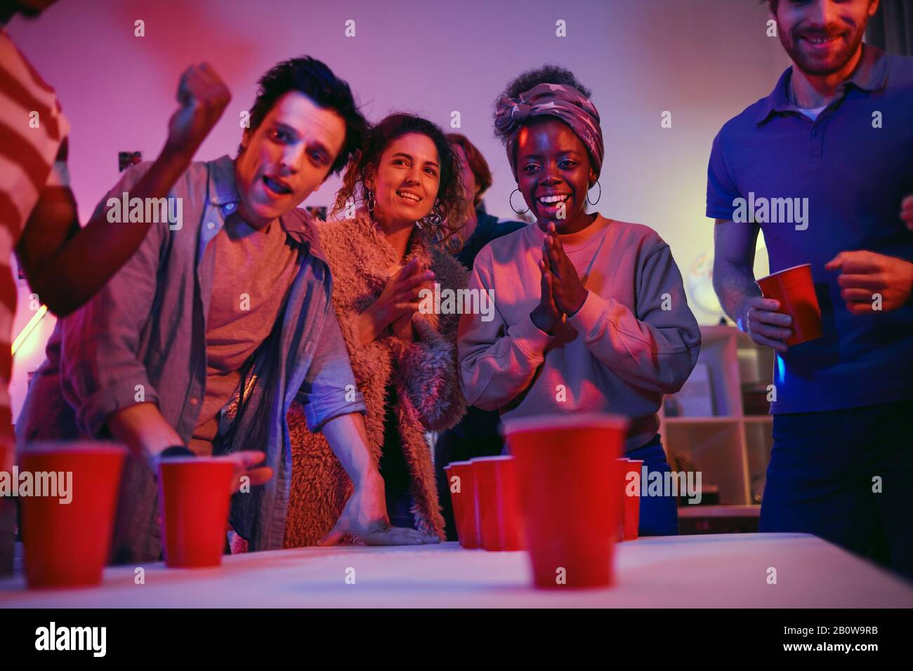 African smiling woman is very excited while playing in beer pong game together with her friends during the party Stock Photo
