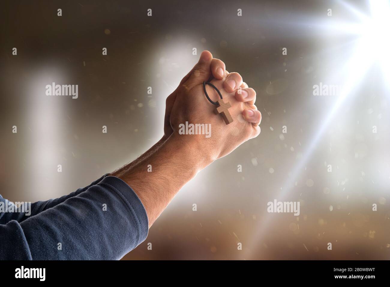 Man praying in church with his hands closed and with pendant with cross symbol in his hand and flash. Horizontal composition Stock Photo