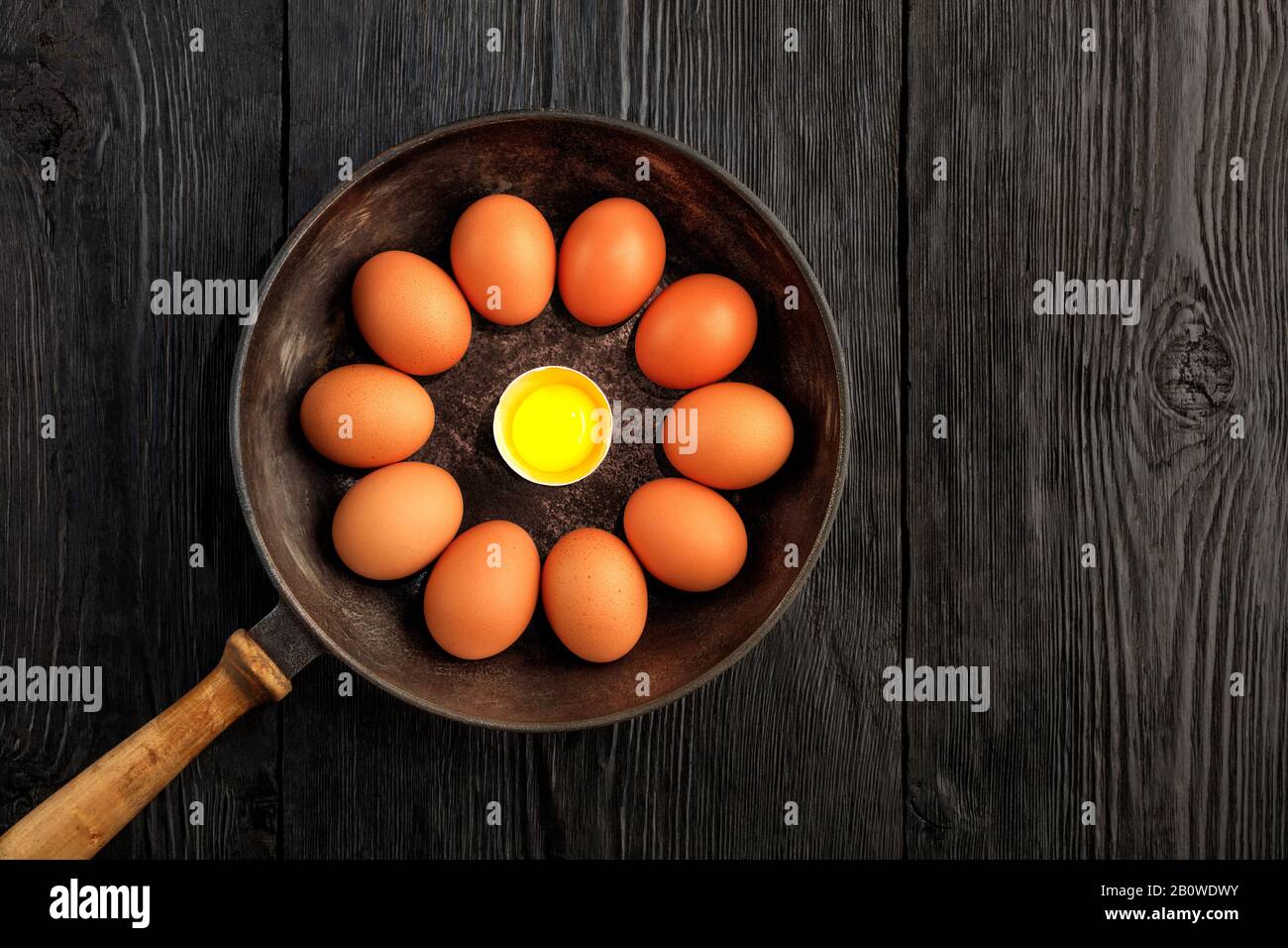Ten brown chicken eggs in an old cast-iron skillet look in the center at a broken egg with a bright yolk. Stock Photo