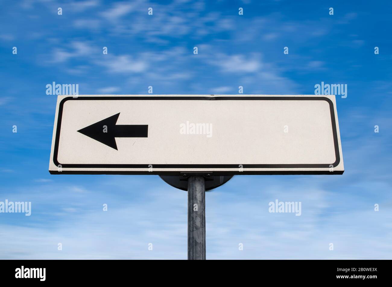 Blank white left directional arrow sign with copy on blue. White road sign with arrow on blue sky with clouds background. Left pointing direction sign Stock Photo