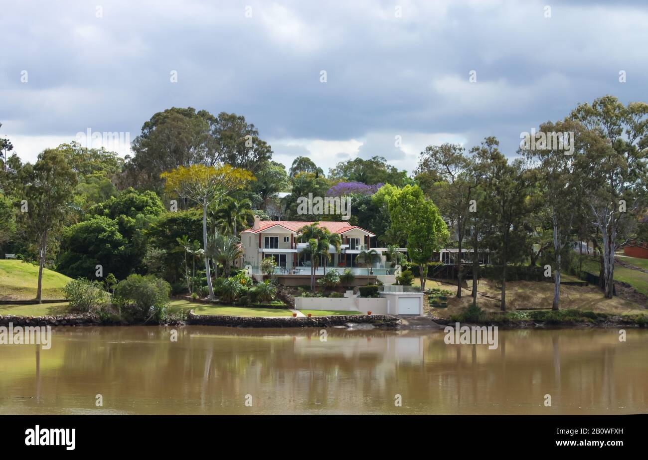 House on the river in Queensland Australia with palms and tall gumn trees under a stormy sky in spring Stock Photo