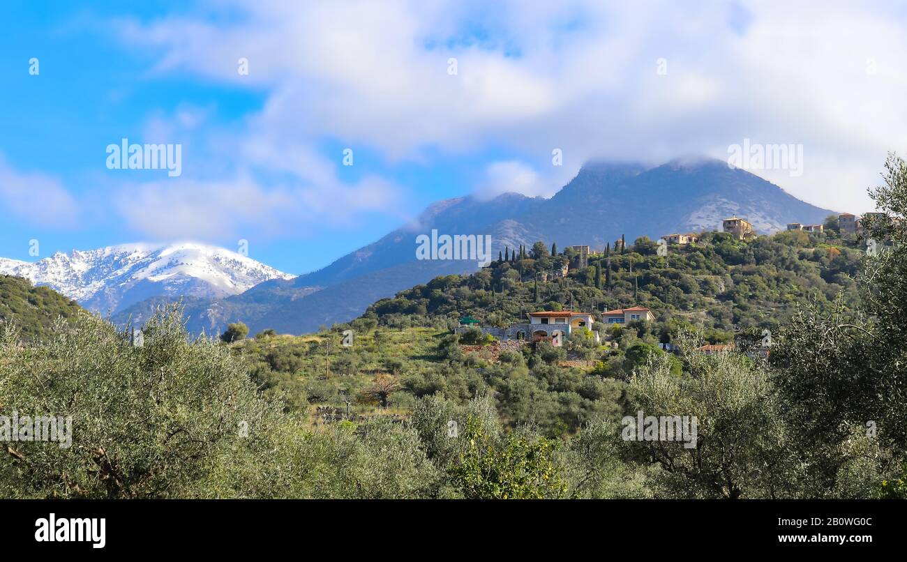 Houses up on the side of a hill in with the snow and fog capped Taygetos mountain range in the distance in Southern Greece Stock Photo