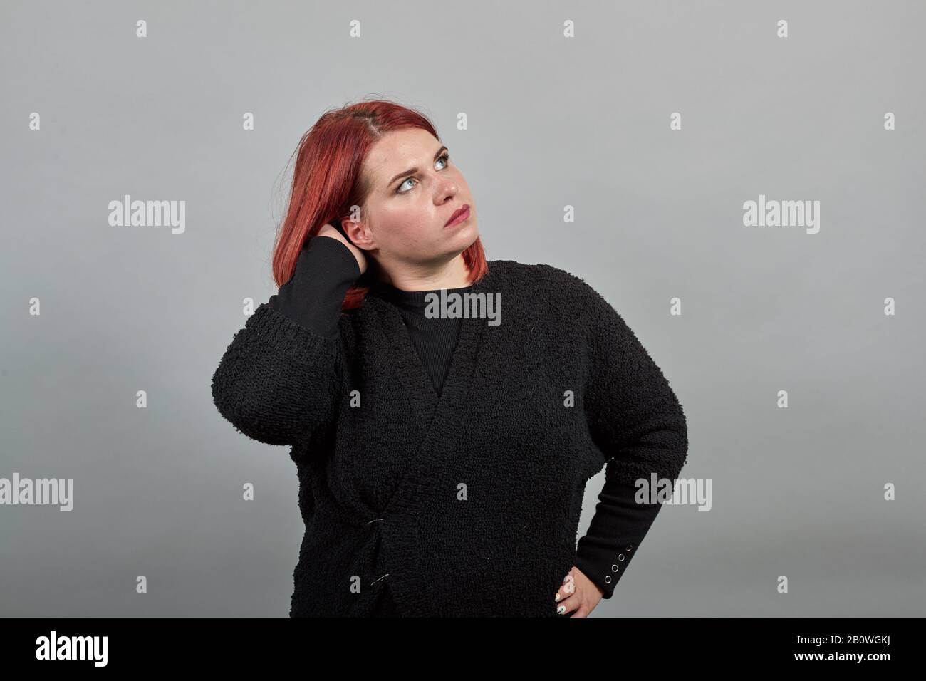 Young redhead fat lady in black sweater smart woman thinks, holds hand over head Stock Photo