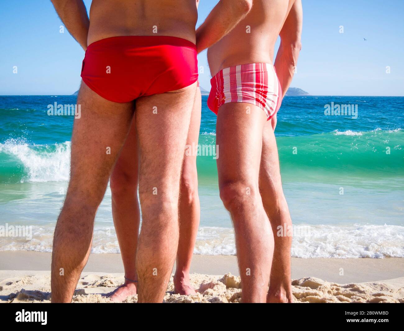 A group of unrecognizable Brazilian men wearing a style of swimwear known locally as 'sunga' standing on the shore of Ipanema Beach in Rio de Janeiro Stock Photo