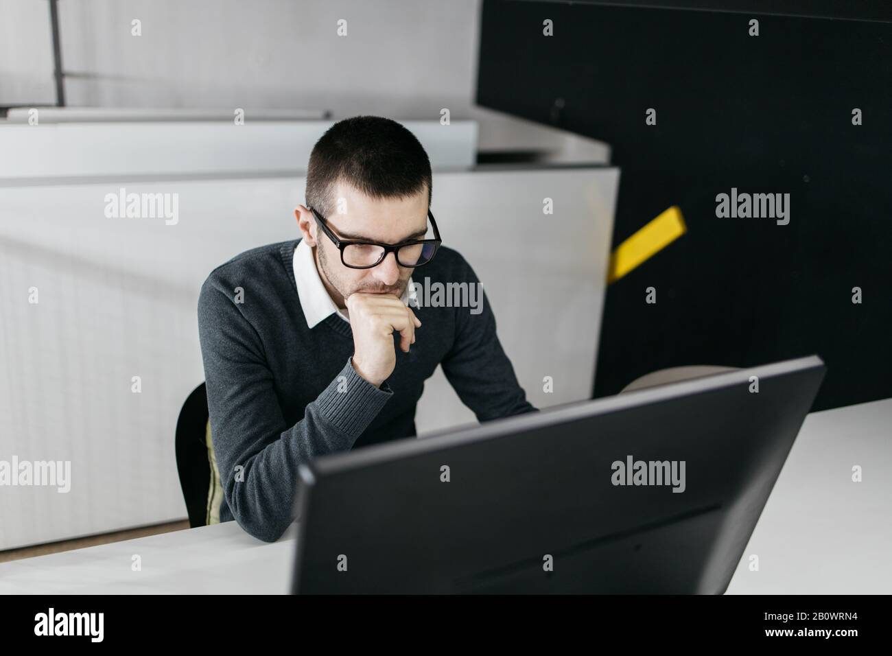 Focused worker searching online studies using computer. Employee with glasses working on computer in the working area. Stock Photo