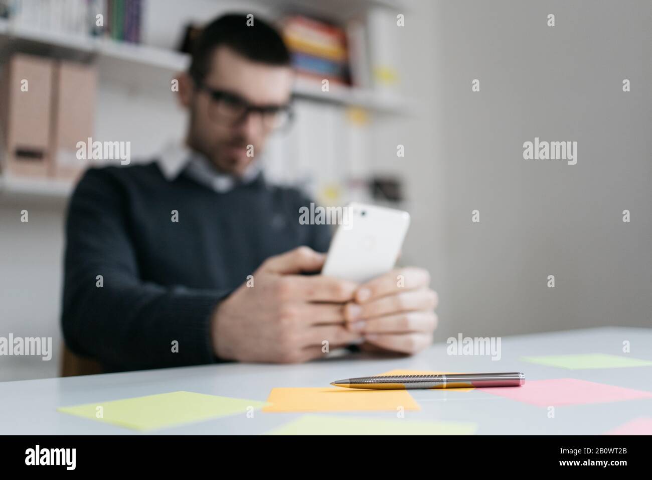 Elegant pen on table with sticky notes. Metal pen with colored sticky notes with blurred man holding on out of focus phone in office Stock Photo