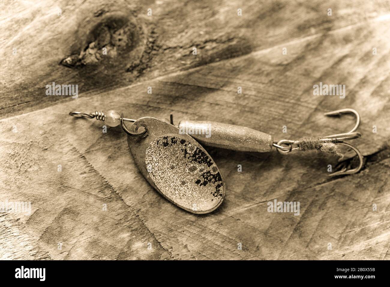 https://c8.alamy.com/comp/2B0X55B/a-metal-spinner-equipped-with-a-treble-hook-that-is-designed-for-catching-predatory-fish-displayed-on-a-piece-of-driftwood-and-sepia-toned-dorset-en-2B0X55B.jpg