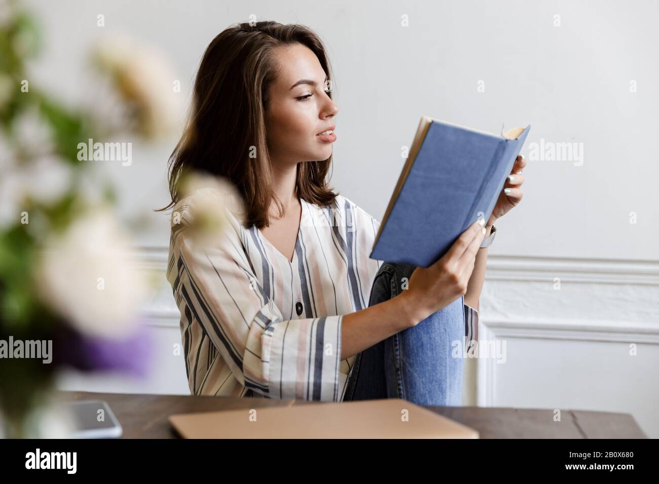 Beautiful smiling young girl sitting at the table at home, reading a ...