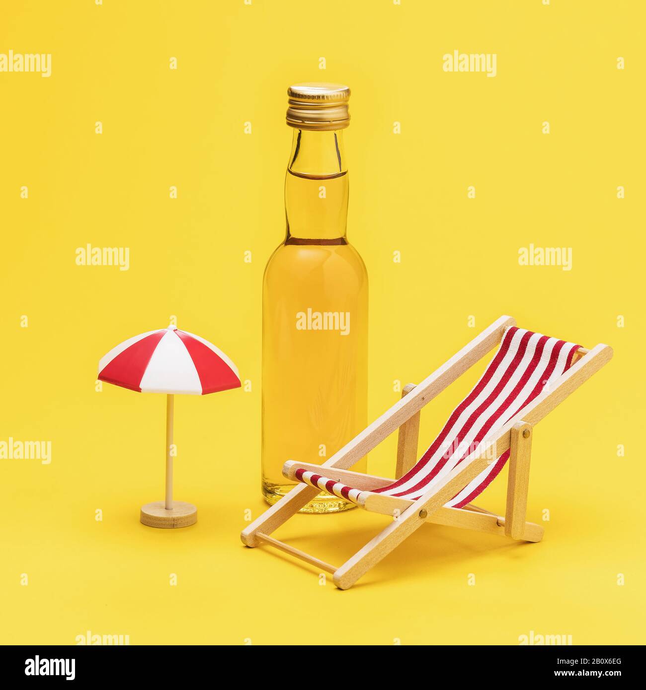 Bottle of whiskey, deck chair and umbrella on a yellow background. Concept on the topic of alcohol abuse on the beach Stock Photo
