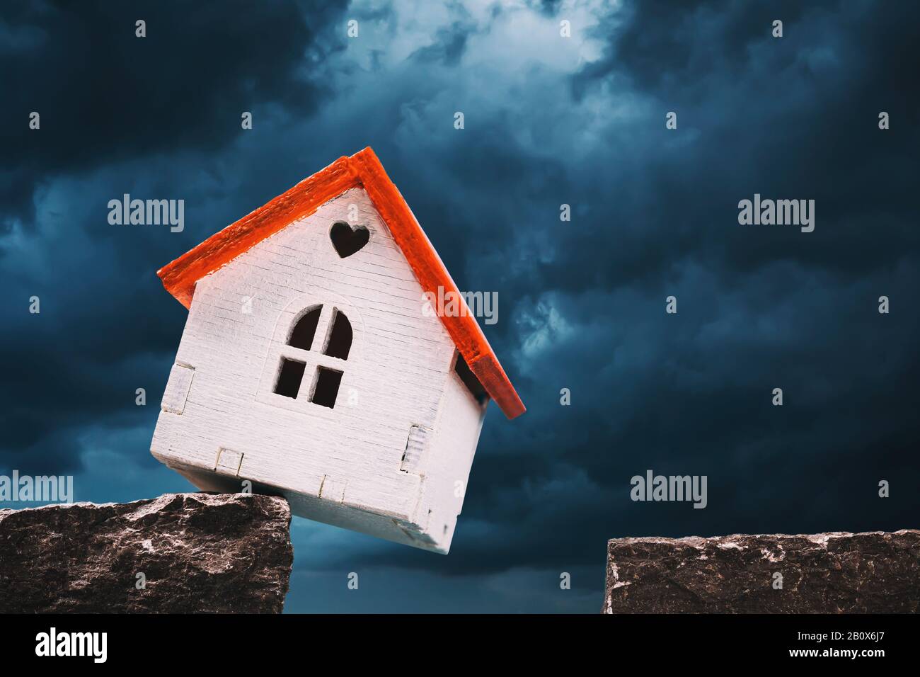 A toy house on a cliff of rock amid a grim sky. Concept on outstanding debt for mortgage lending Stock Photo