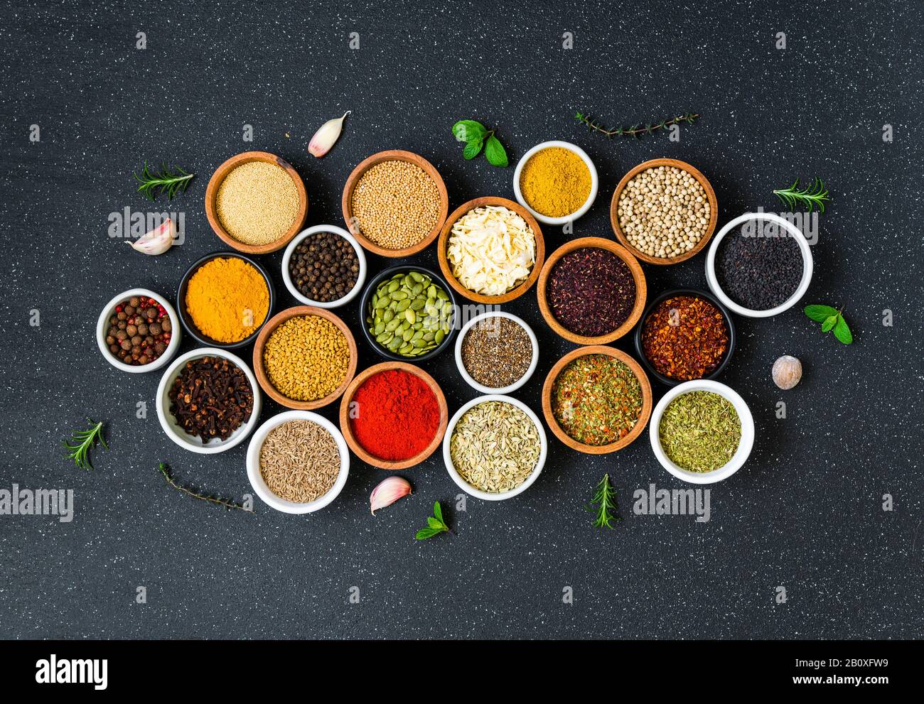 Variety of colorful spices, herbs, and seeds on black stone background. Stock Photo