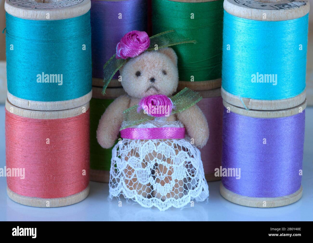 Miniature bear in lace and flowers surrounded by spools of pastel colored thread. Stock Photo