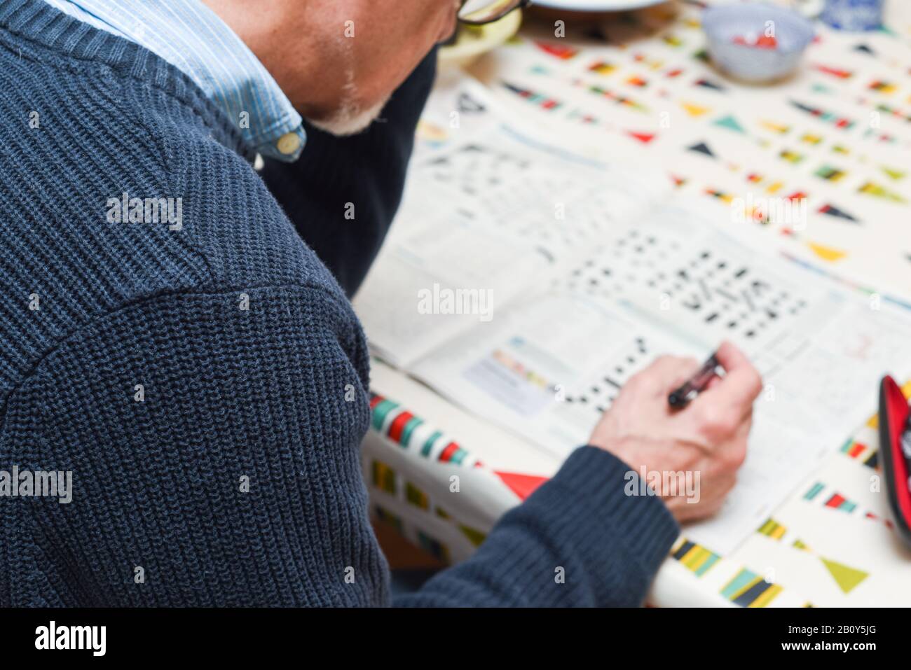 Mature man doing a crossword puzzle and relaxing at home during the day, indoor shot Stock Photo