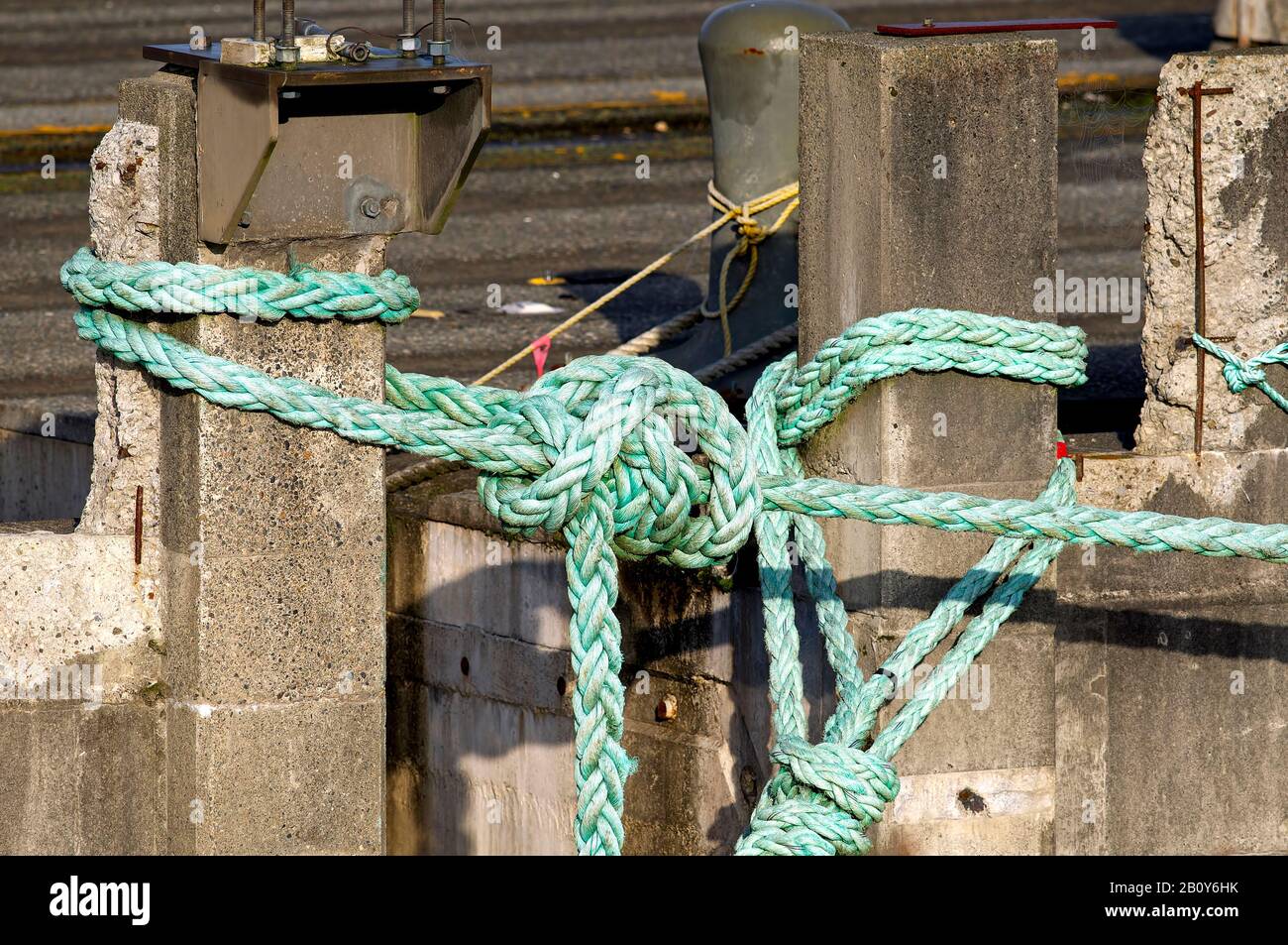A knotted green nylon rope tied around two cement pillars. Stock Photo