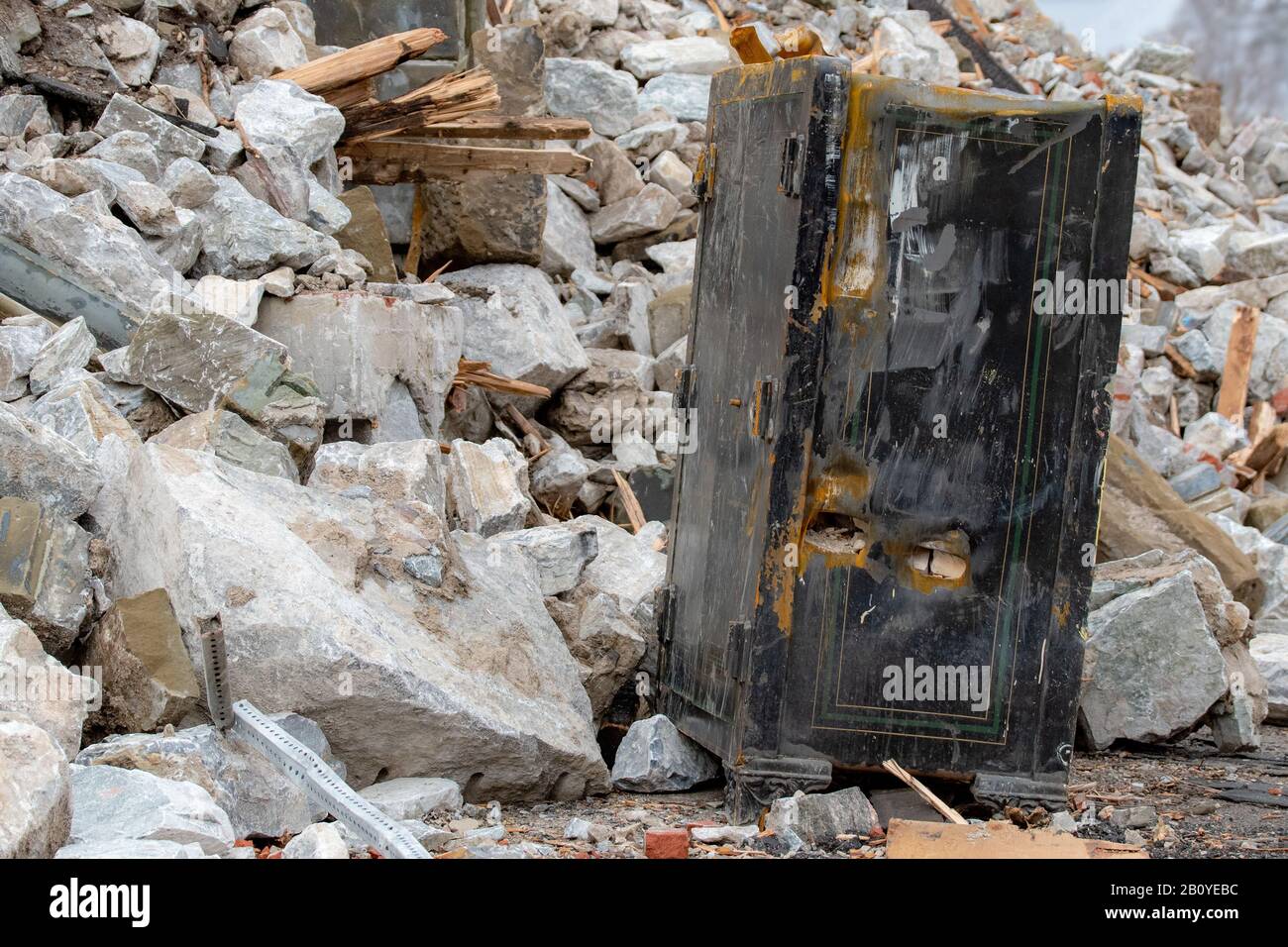 An old floor standing safe in front of a pile of rubble. The save is damaged and the dial is missing, but it is still closed. Stock Photo