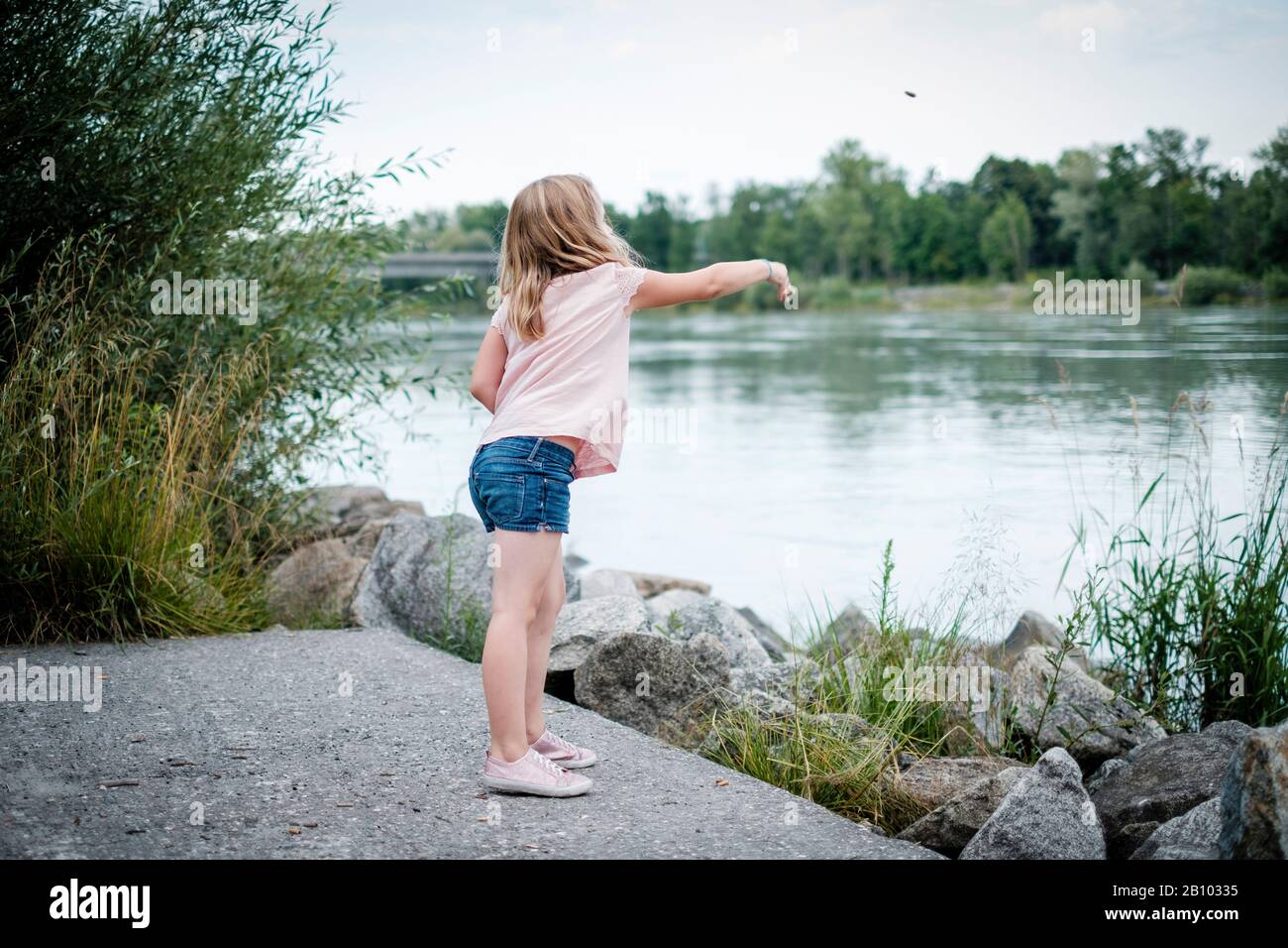 Little girl throws stones into a river hires stock photography and