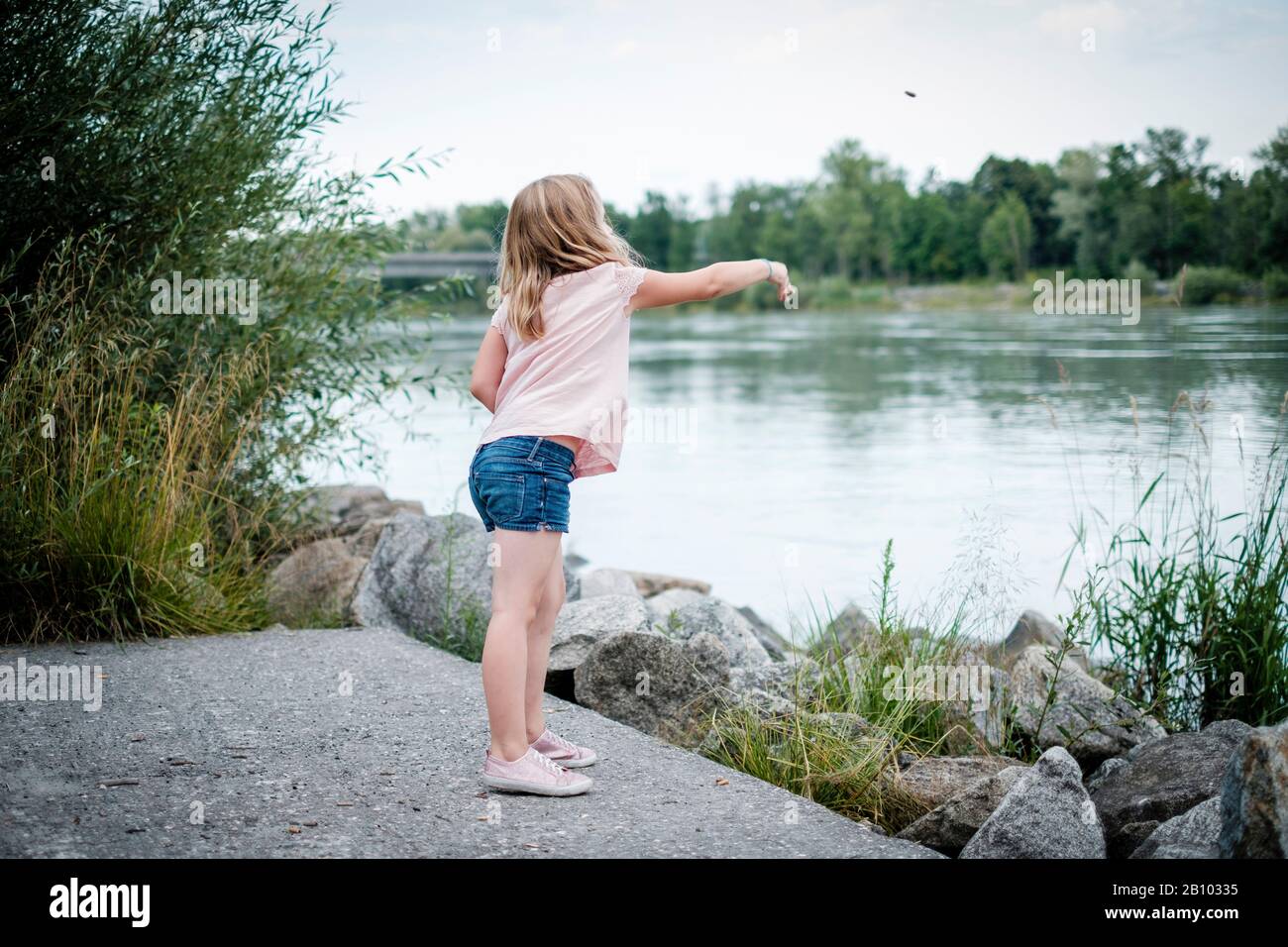 Little girl throws stones into a river Stock Photo