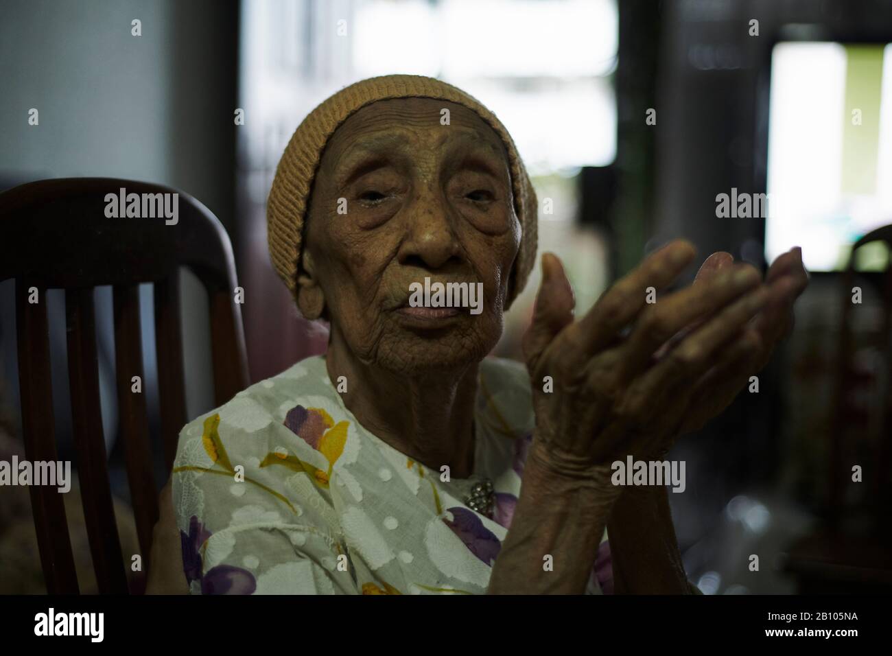 Portrait of an elderly Malay woman sitting on a chair in her living ...