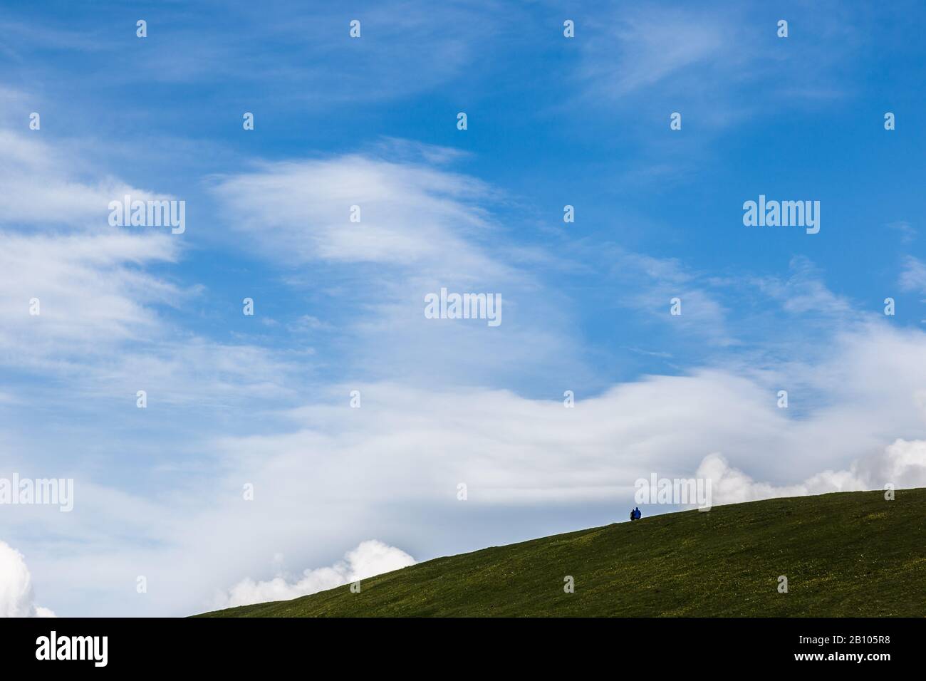 Mountains view in spring with green meadows, blue sky and two distant people Stock Photo