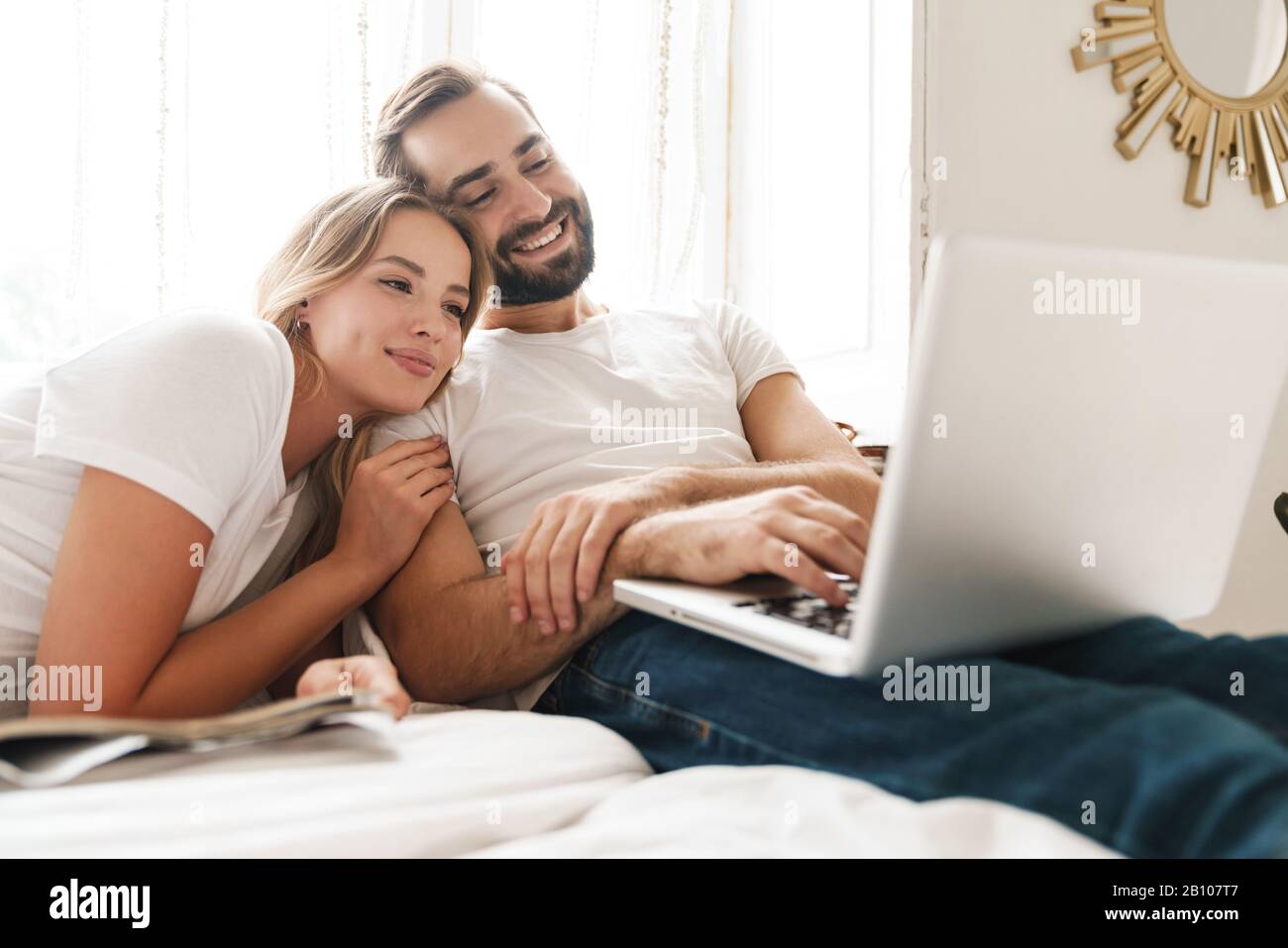 Beautiful happy young couple relaxing on bed at home, watching movies ...