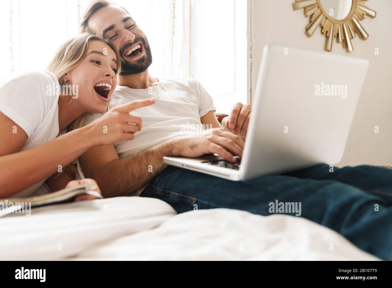 Beautiful happy young couple relaxing on bed at home, watching movies ...